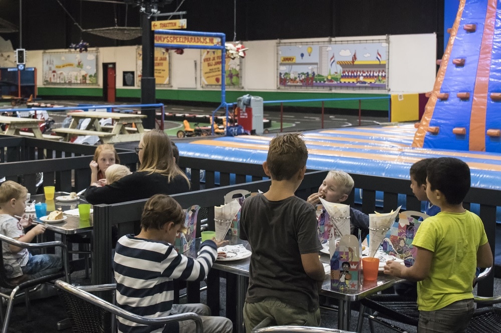 Kinderen aan het eten op het terras met uitzicht op het speelparadijs met het springkussen.